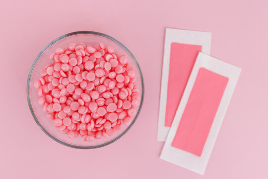 Beautiful pink wax granules and wax depilatory strips for delicate areas on a pink background. Epilation, depilation, unwanted hair removal. Top view.