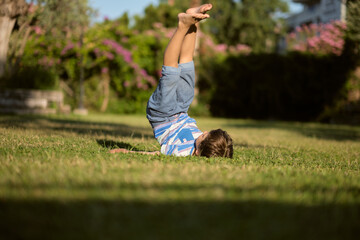 Mischievous preschooler boy somersaults on sand grass in the park.