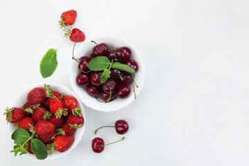 Two white plates with cherries and strawberries with mint petals stand on a white background with space for text. High quality photo