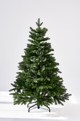 Artificial Christmas green tree without decorations on a metal stand isolated on a white background.