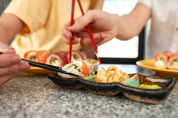 Beautiful caucasian mom and two daughters eating rolls and sushi at family lunch at home. Delivery food. Traditional japanese food.