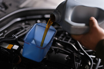 Fototapeta premium Auto mechanic replaces and pours fresh oil into engine at service station