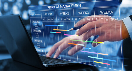 Project manager working on laptop and updating tasks and milestones progress planning with Gantt...