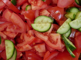 Large red delicious tomatoes and fresh cucumbers sliced for salad. Vitamin food for vegetarians, ready to eat. Ripe fragrant vegetables without spices.