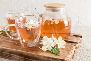 Front view of a modern double bottom glass cup with delicious jasmine tea, glass teapot and flowers on a wooden board.