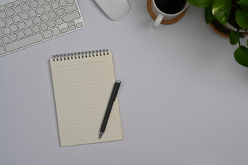 Blank notepad, coffee cup, keyboard and potted plant on white office desk