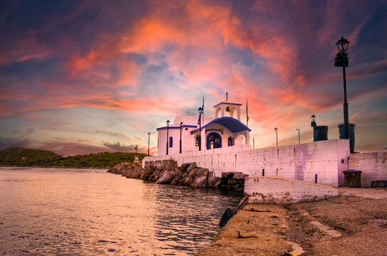 Greek small chapel with white roofs on cliff over sea and small bay under a dramatic sky at sunset