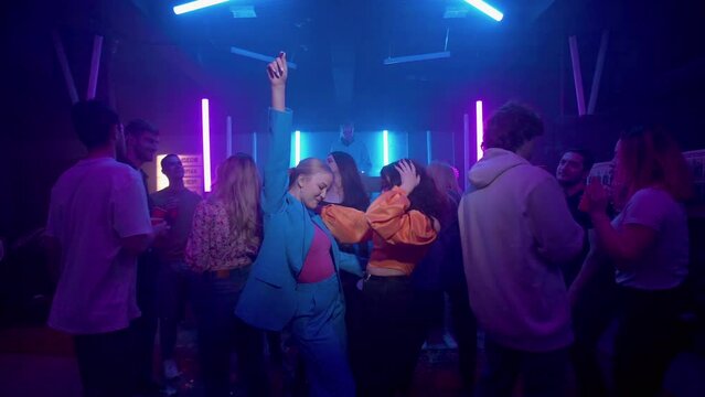 Lesbian girls dance among the crowd in a nightclub under the illumination of colored spotlights. Night club. LGBT