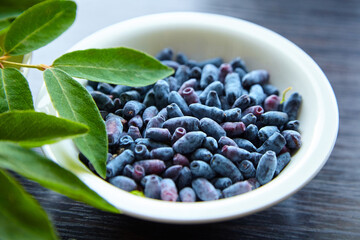 Summer honeysuckle berries with fresh leaves in white plate over wooden table