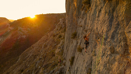AERIAL: Woman climbing up the limestone wall with golden sun flare in background