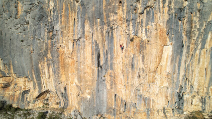 AERIAL: Gorgeous sunlit limestone wall with ascending young female rock climber