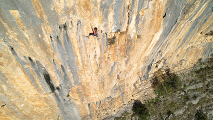 AERIAL: Sporty young woman top rope climbing up the picturesque limestone wall