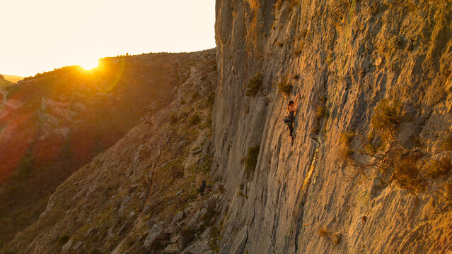 AERIAL: Woman climbing in the middle of the wall with sun flare in background