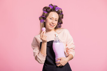 Smiling woman promotes laundry detergent on pink studio background sniffs fabric softener with...