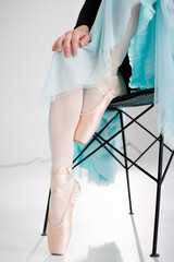 Ballerina in pointe shoes. Ballet posing, performance. Woman's legs with shoes for ballet dancing. Girl in green skirt on chair © Dmitriy