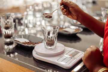 Close up of African American female worker weighing coffee beans for tasting while using scales