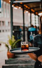 waitress standing in outdoor cafe. girl the waiter holds a tray with a glass of alcoholic cocktail