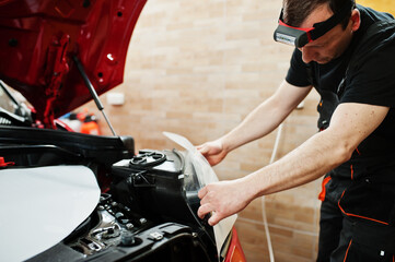 Car service worker put anti gravel film on a red car body at the detailing vehicle workshop. Car protection with special films.