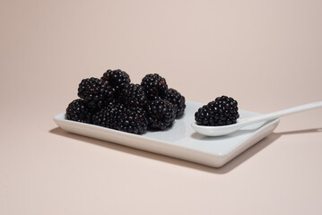 Ripe blackberries on a white plate on a light background.