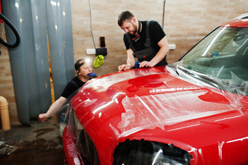 Car service worker put anti gravel film on a red car body at the detailing vehicle workshop. Car...