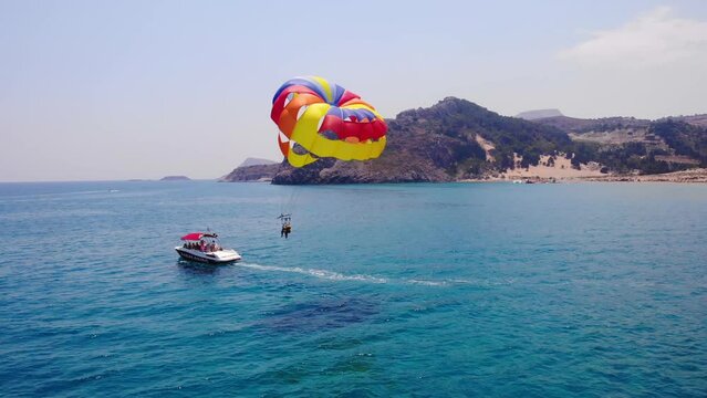 Parasailing, Tourists On Parachute Towed Behind The Speedboat In Tsambika Beach, Greece. - aerial