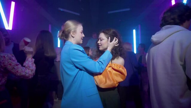 Lesbian girls approach each other and kiss among the crowd in a nightclub under the light of colored spotlights. Night club. LGBT