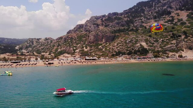 Paraskiing - Vacationist Ride On Canopy Connected To Speedboat Crusing In The Blue Sea Near Tsambika Beach In Greece. - aerial