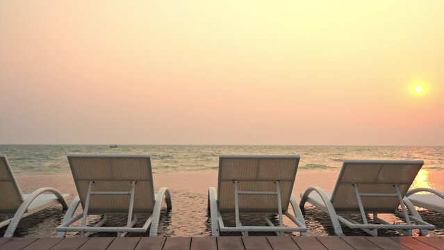 A row of beach loungers sits in shallow water facing the incoming tide at sunset. Title space