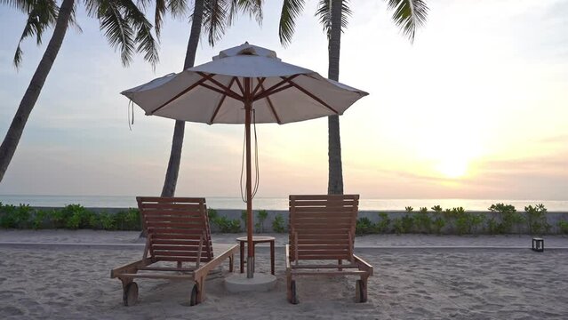 Two empty sun loungers face out on a tropical ocean sunset.