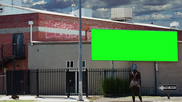 Girl Billboard Green Screen House Outdoor. Woman standing in the street looking to an outdoor billboard green screen hanging in front of a house