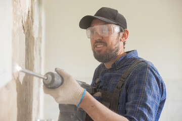Mature man wearing baseball cap with safety glasses and gloves works on renovation demolition of...