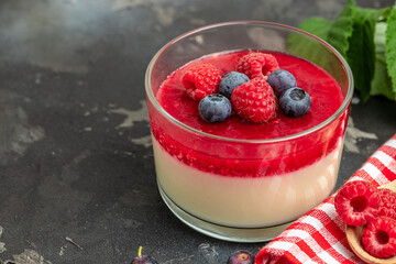 Delicious italian dessert panna cotta with berry sauce on a dark background in small jars. place...