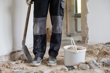 Close up shot of the legs of a man in a protective suit with a shovel in hand next to a bucket of...