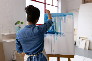 Image of back view of biracial female artist working on painting in studio