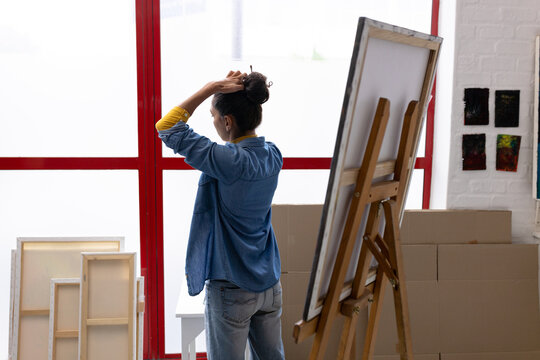 Image of biracial female artist looking outside window in studio