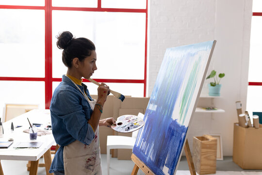 Image of biracial female artist working on painting in studio