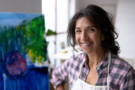 Image of happy biracial female artist working on new painting in studio