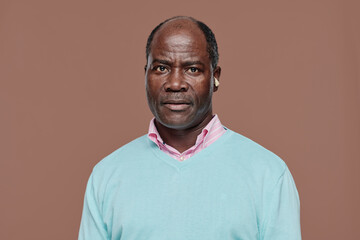Obraz premium Portrait of African senior man with deafness in blue shirt looking at camera against beige background