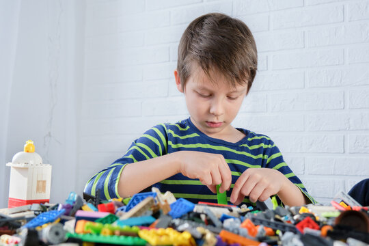 A Boy Sits At A Table In Front Of Scattered Multi-colored Building Blocks. The Child Enthusiastically Builds Something, Develops Fantasies, Children's Leisure.