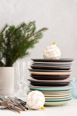 Preparing for a festive table setting, a stack of different plates and forks with knives, fir branches in a concrete vase, Christmas balls and decorations