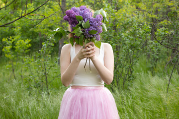 girl in forest with lilac bouquet in pink skirt