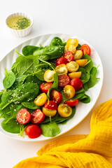 Salad with yellow and red tomatoes and spinach, top view of an oval plate with lettuce on a white background