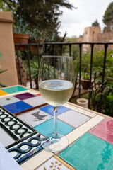 Glass of Spanish dry white wine served on outdoor terrace with view on red walls of Andalusian fortress Alhambra in Granada, Spain