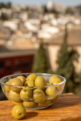 Obraz na płótnie Canvas Glass bowl with green andalusian olives served on outdoor terrace with view on old part of Granada, Andalusia, Spain