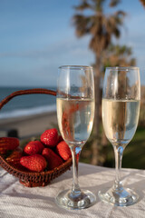 Glasses of Spanish cava sparkling wine with fresh ripe strawberry and view on blue sea and sandy beach, Costa del Sol vacation destination, Andalusia, Spain