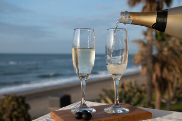 Pouring of Spanish cava sparkling wine is glasses with view on blue sea and sandy beach, Costa del...