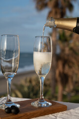 Pouring of Spanish cava sparkling wine is glasses with view on blue sea and sandy beach, Costa del Sol vacation destination, Andalusia, Spain