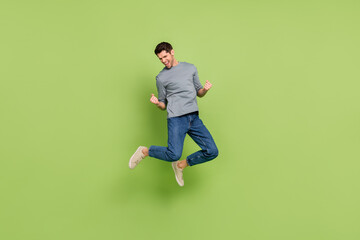 Full size photo of cheerful laughing man jumping raise fists in success triumph isolated on green...