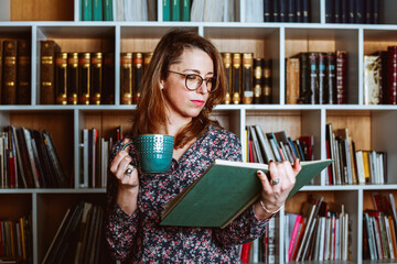 Woman at the library reading a book and holding a cup of coffee. Business girl at the office 