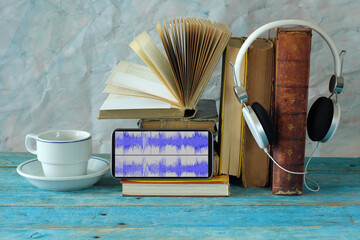 audio book concept with stack of books, headphones,smartphone displaying audio waveform and cup of...